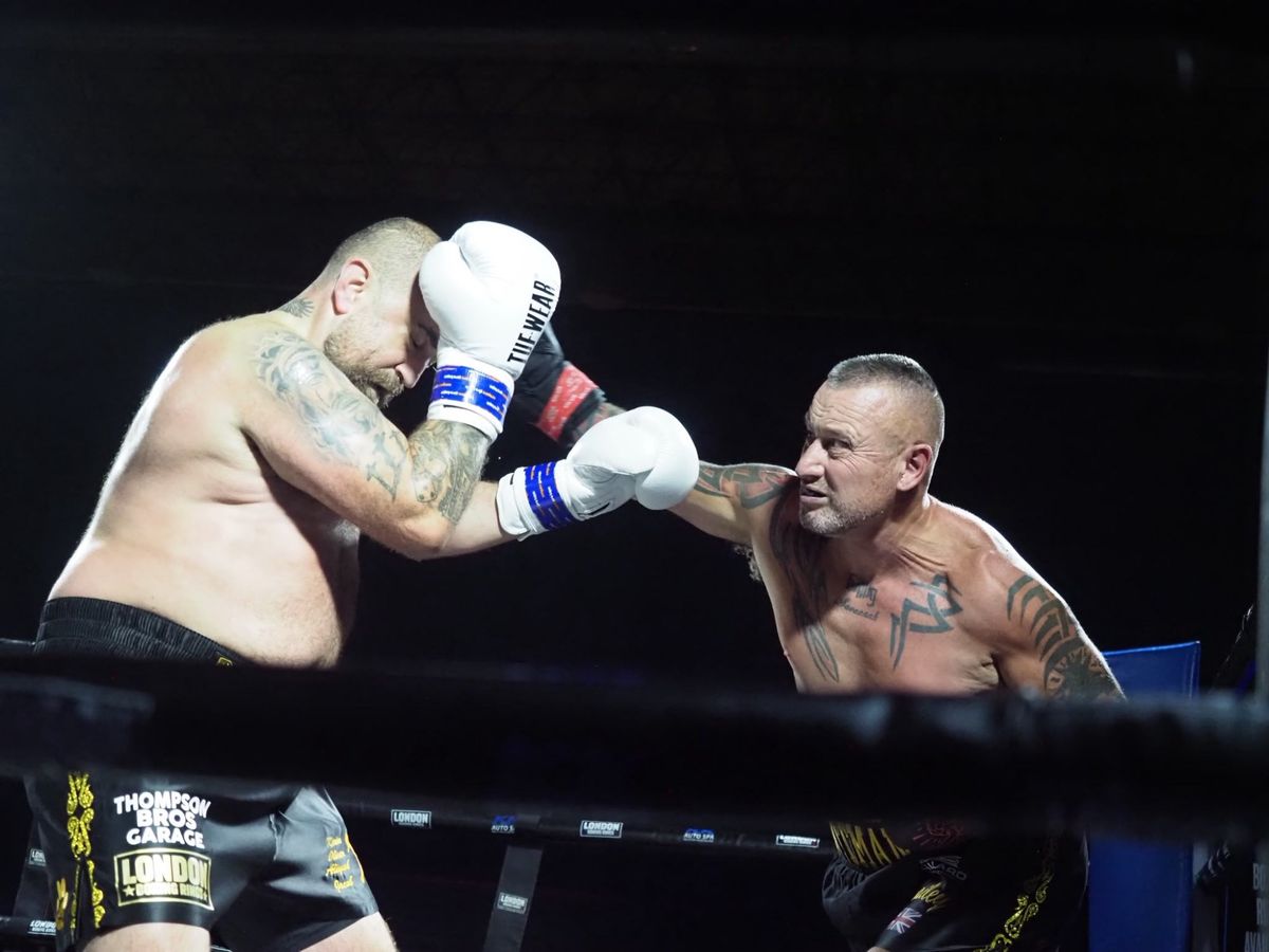 Two heavyweight fighters trade punches against the ropes